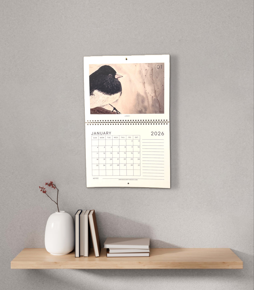 Wall calendar with a bird illustration on a wooden shelf against a gray wall