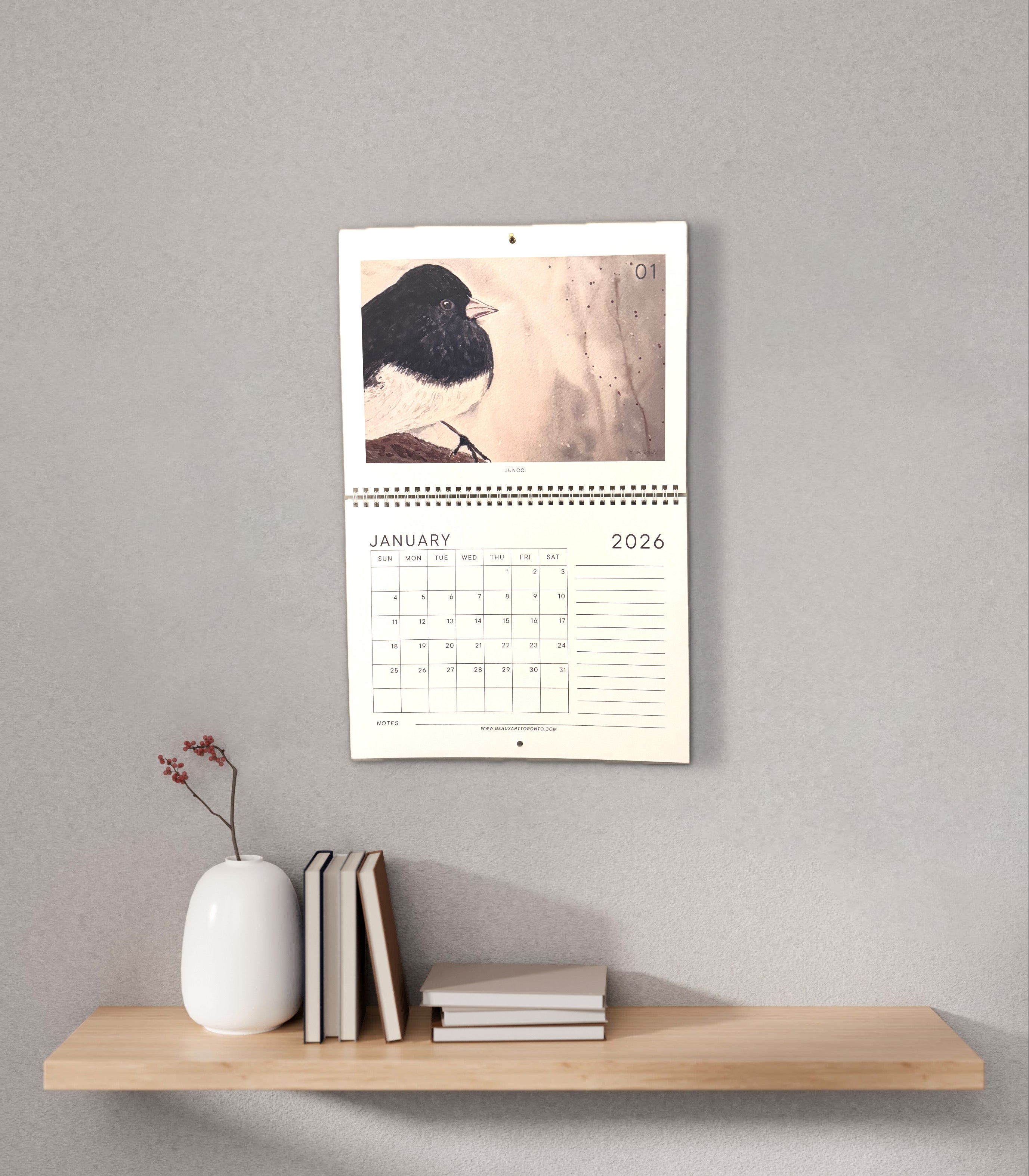 Wall calendar with a bird illustration on a wooden shelf against a gray wall